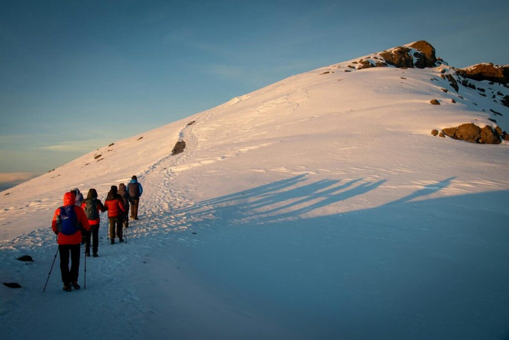 A group of hikers trekking a snowy mountain path at sunrise.